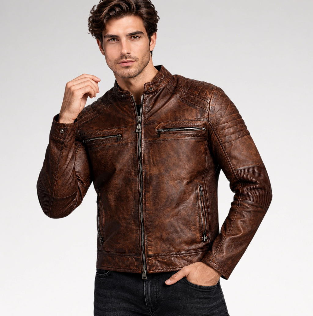 A man wearing a distressed brown leather motorcycle jacket with a front zipper, zippered chest pockets, and ribbed panels on the shoulders and sleeves, posed against a light gray studio background.