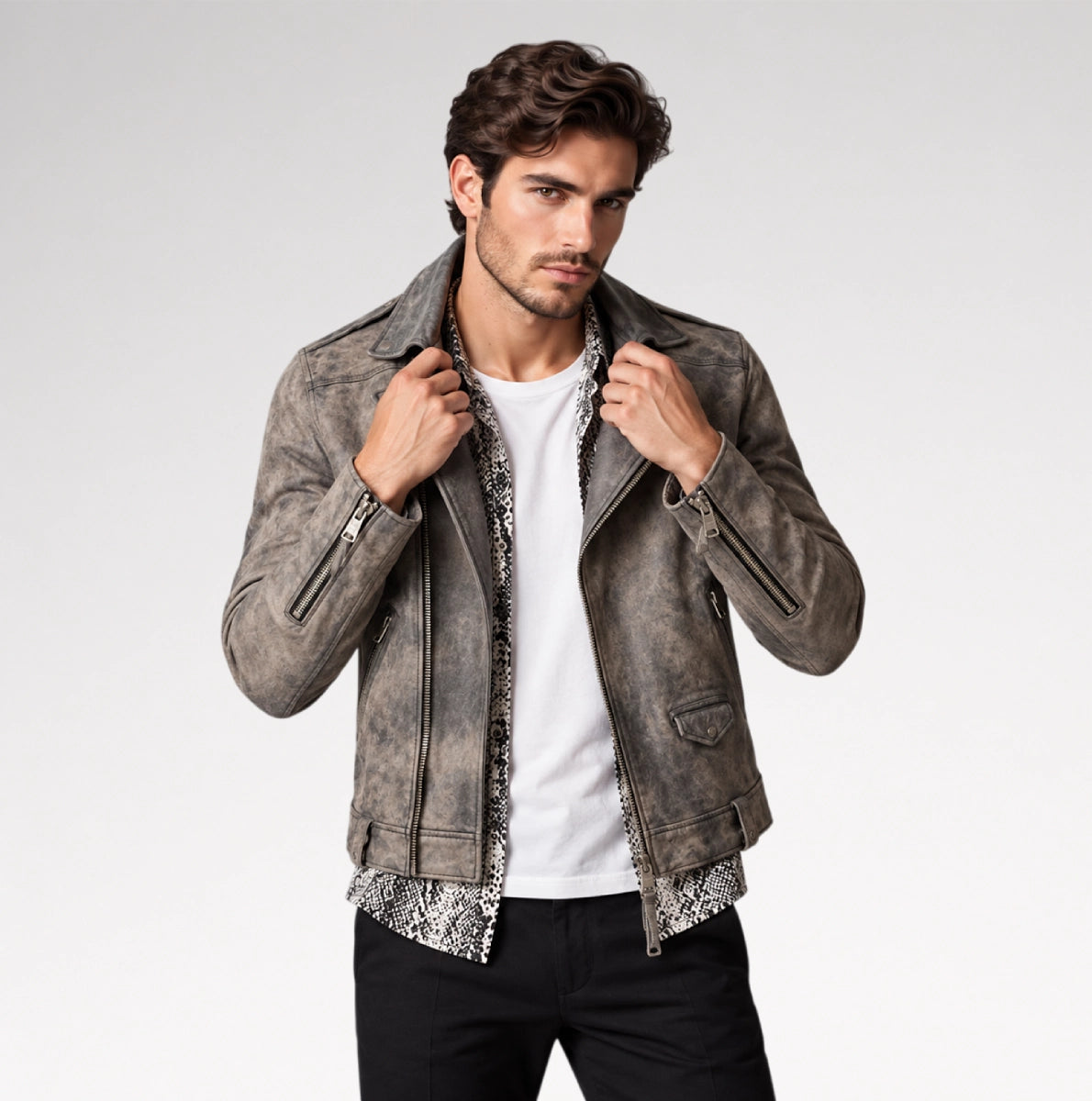 A man wearing a distressed gray leather jacket over a white t-shirt and black pants, posing against a light gray studio background.