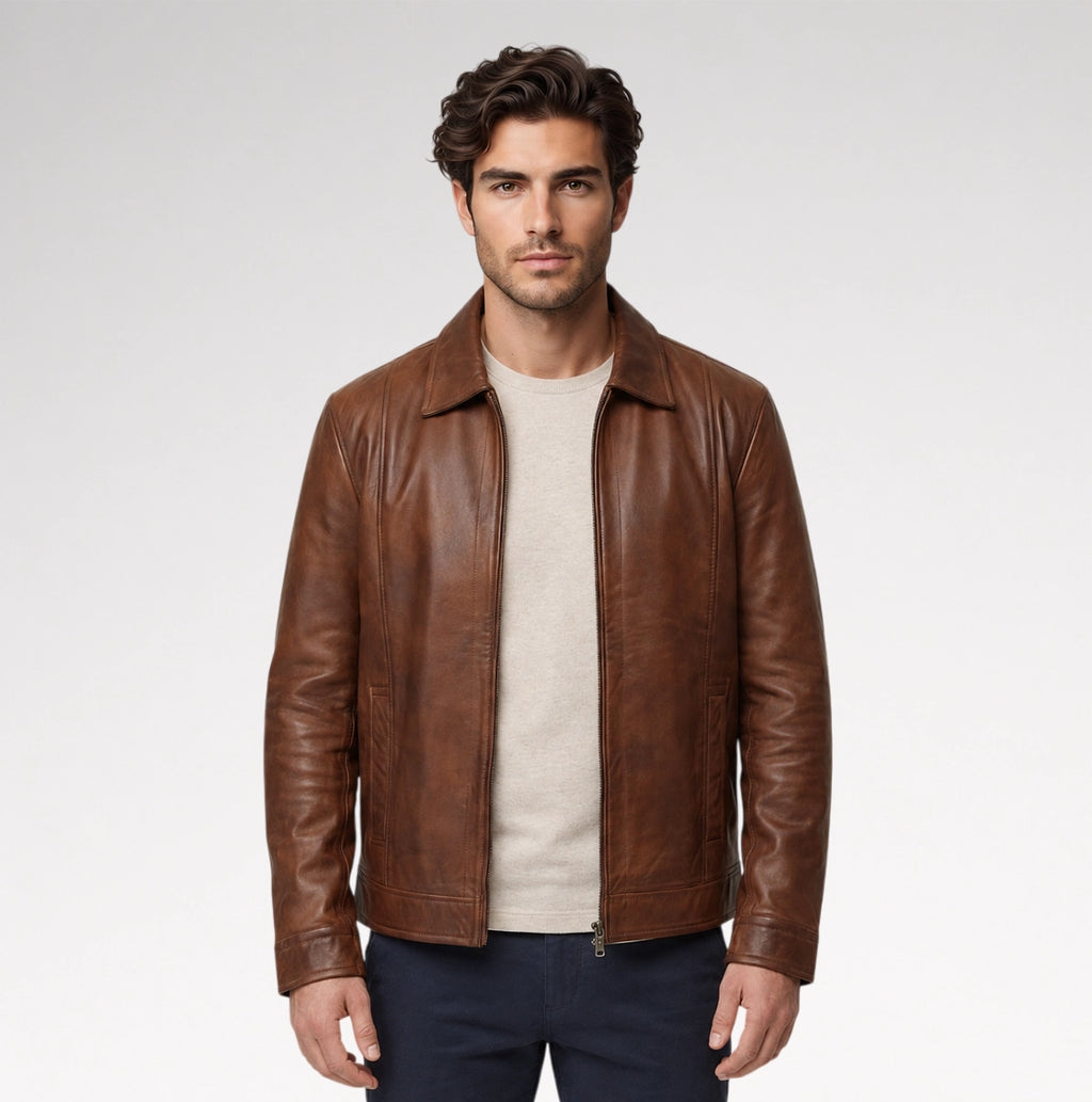 A man wearing a brown leather jacket over a beige T-shirt and dark pants, standing against a light gray studio background.