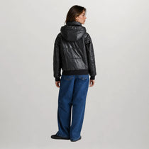 A model shown from the back wearing a black puffer jacket with a hood and wide-leg blue jeans, photographed against a neutral light gray studio background.