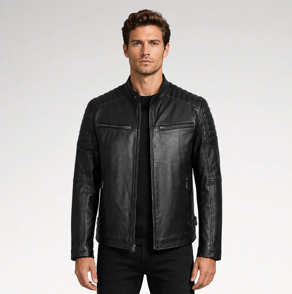 A man wearing a black leather jacket with quilted shoulder panels, zippered chest pockets, and a ribbed hem, photographed against a light gray studio background.