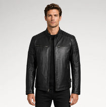 A man wearing a black leather jacket with quilted shoulder panels, zippered chest pockets, and a ribbed hem, photographed against a light gray studio background.