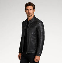 A man wearing a black leather motorcycle jacket with quilted shoulder panels and zippered pockets, photographed against a light gray studio background.