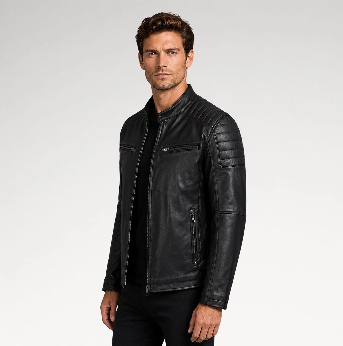 A man wearing a black leather motorcycle jacket with quilted shoulder panels and zippered pockets, photographed against a light gray studio background.