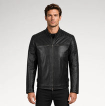 A man wearing a black leather motorcycle jacket with a stand collar, zippered chest pockets, and quilted shoulder panels, photographed against a light gray studio background.
