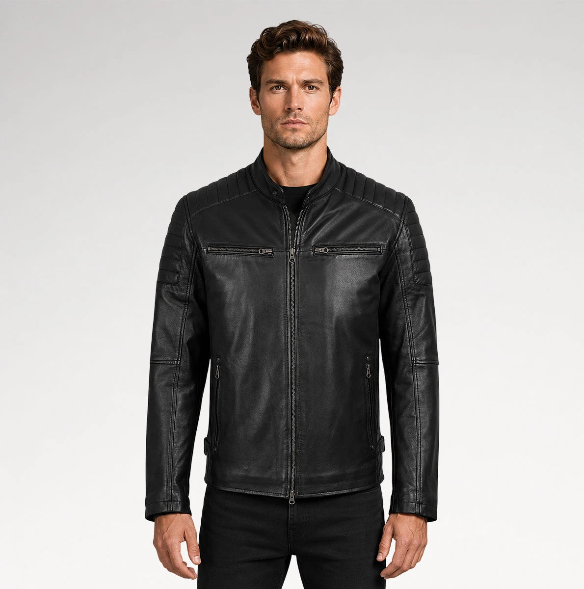 A man wearing a black leather motorcycle jacket with a stand collar, zippered chest pockets, and quilted shoulder panels, photographed against a light gray studio background.