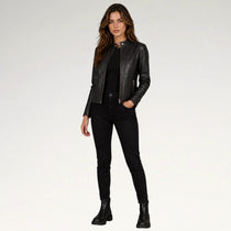 A woman modeling a black faux-leather moto jacket over a black top and black skinny jeans, paired with black ankle boots, against a plain white studio background.