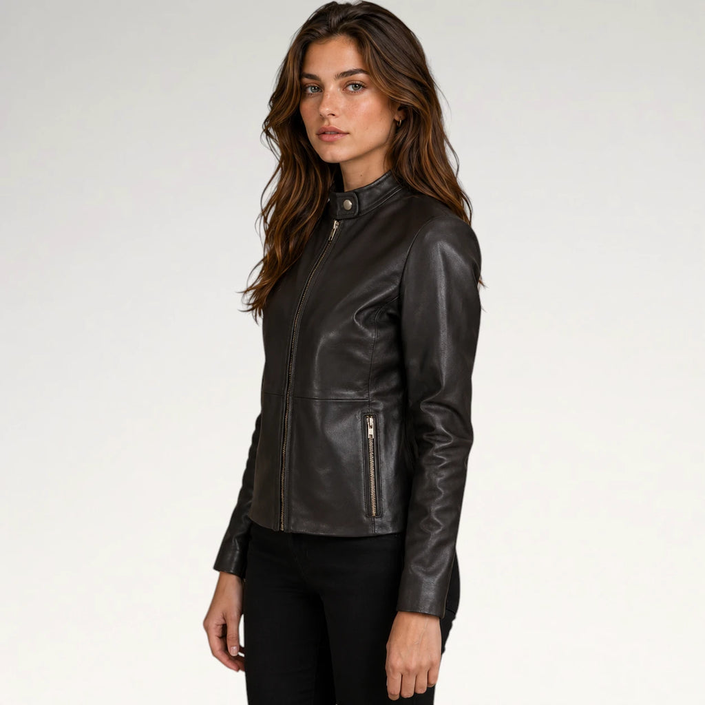 A woman modeling a black leather jacket with a mock neck, front zipper, and zippered side pocket, paired with black pants against a light gray studio background.