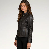 A woman modeling a black leather jacket with a mock neck, front zipper, and zippered side pocket, paired with black pants against a light gray studio background.