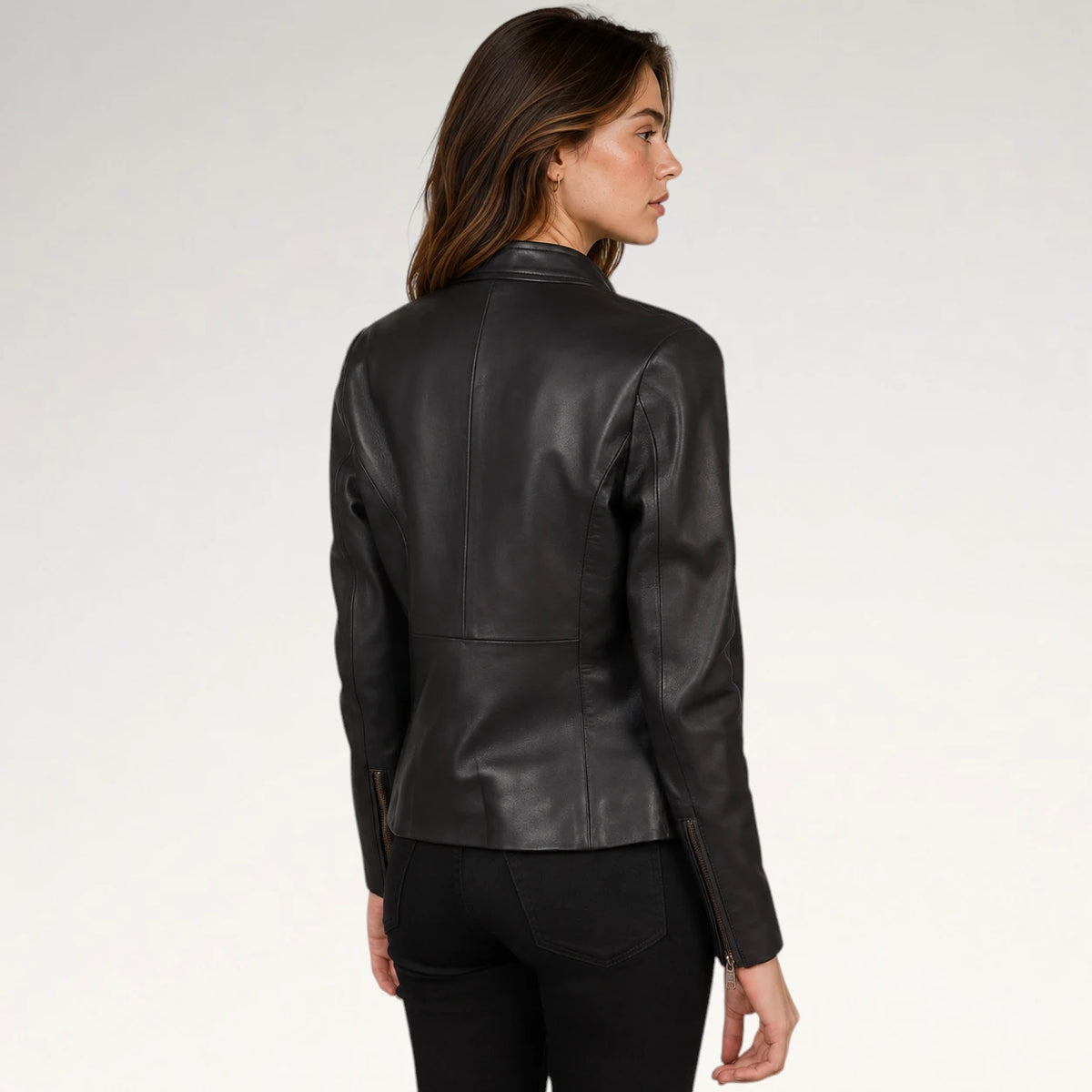 A woman shown from the back wearing a fitted black leather jacket with zip details at the cuffs, paired with black pants, against a plain light gray studio background.