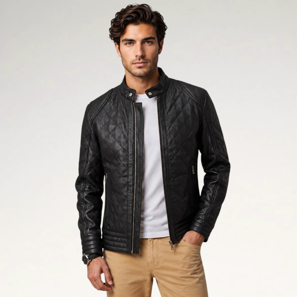 A man wearing a black quilted leather jacket over a white t-shirt and khaki pants, standing against a light gray studio background.