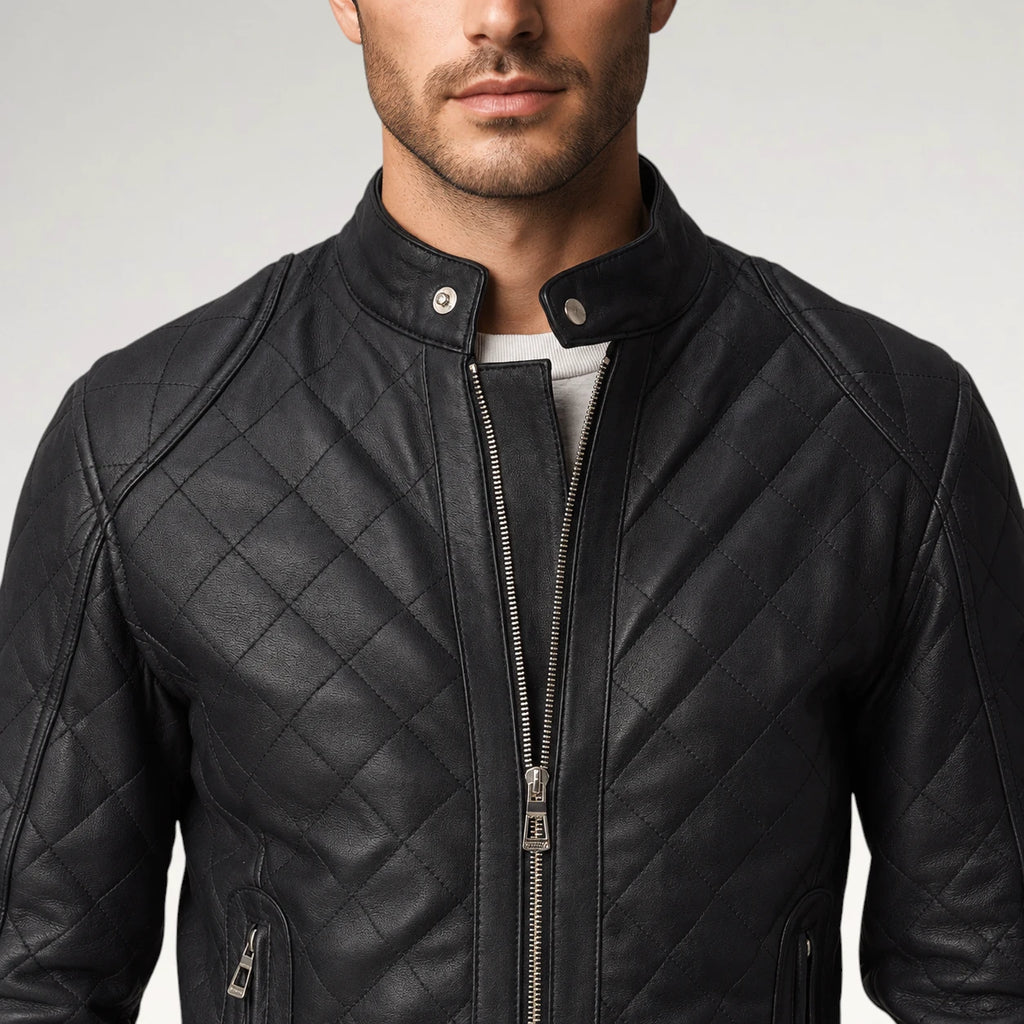 A close-up of a man wearing a black quilted leather jacket with a stand-up collar, silver zipper, and snap-button placket, paired with a light gray shirt.