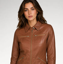 A woman wearing a brown faux leather jacket with a collar, front zipper, and zippered chest pockets, photographed against a light gray studio background.