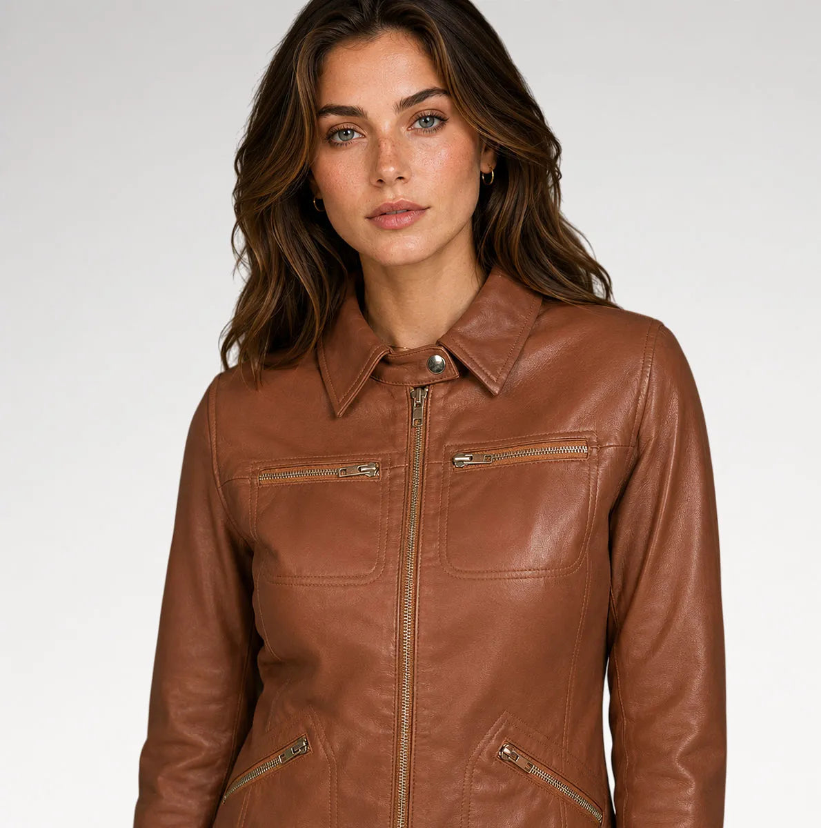 A woman wearing a brown faux leather jacket with a collar, front zipper, and zippered chest pockets, photographed against a light gray studio background.