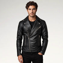 A man wearing a black leather moto jacket with silver zippers, styled over a black t-shirt and black pants, photographed against a light gray studio background.