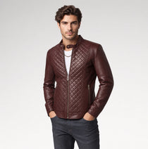 A man wearing a dark brown quilted leather jacket over a white t-shirt and dark gray jeans, standing against a light gray studio background.