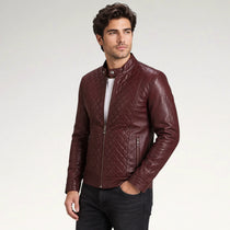 A man wearing a burgundy quilted faux leather jacket, styled with a white t-shirt and black jeans, standing against a light gray studio background.