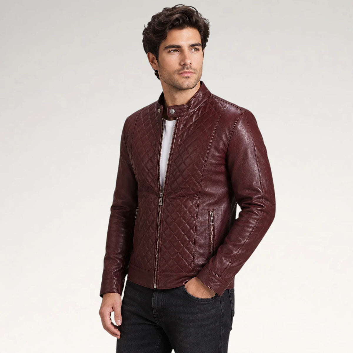A man wearing a burgundy quilted faux leather jacket, styled with a white t-shirt and black jeans, standing against a light gray studio background.