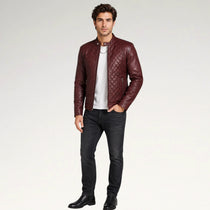A man modeling a burgundy quilted leather jacket over a white t-shirt and black jeans, standing against a light gray studio background.