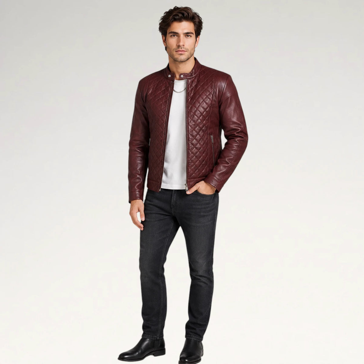 A man modeling a burgundy quilted leather jacket over a white t-shirt and black jeans, standing against a light gray studio background.