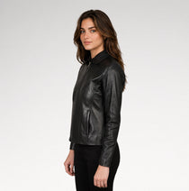 A woman wearing a black leather jacket with a collar and front zipper, shown in profile against a light gray studio background.