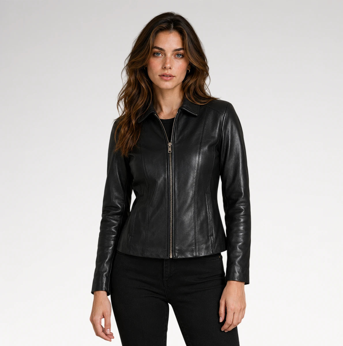 A woman modeling a black faux-leather zip-front jacket with a collar and long sleeves, paired with black pants, against a light gray studio background.