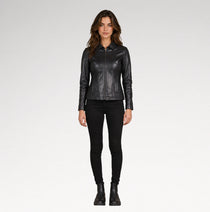 A woman modeling a black leather jacket with a collar and front zipper, paired with black skinny pants and black ankle boots, against a light gray studio background.