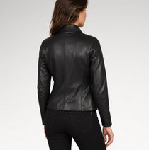A woman viewed from the back wearing a fitted black leather jacket and black pants against a light gray studio background.