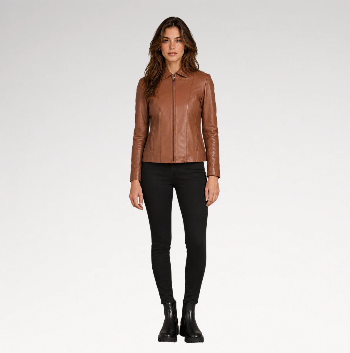 A woman modeling a brown leather jacket with a collar and front zipper, paired with black skinny pants and black ankle boots, against a light gray studio background.
