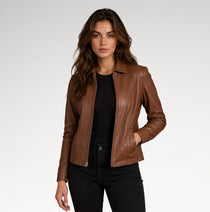 A woman modeling a brown faux-leather moto jacket over a black top and black pants, photographed against a light gray studio background.