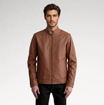 A man wearing a brown leather jacket with a stand collar and front zipper, paired with black pants, photographed against a light gray studio background.