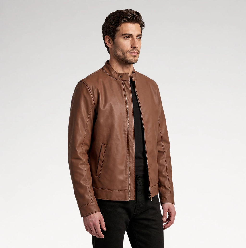 A man wearing a brown leather jacket over a black shirt and black pants, photographed against a plain light gray studio background.
