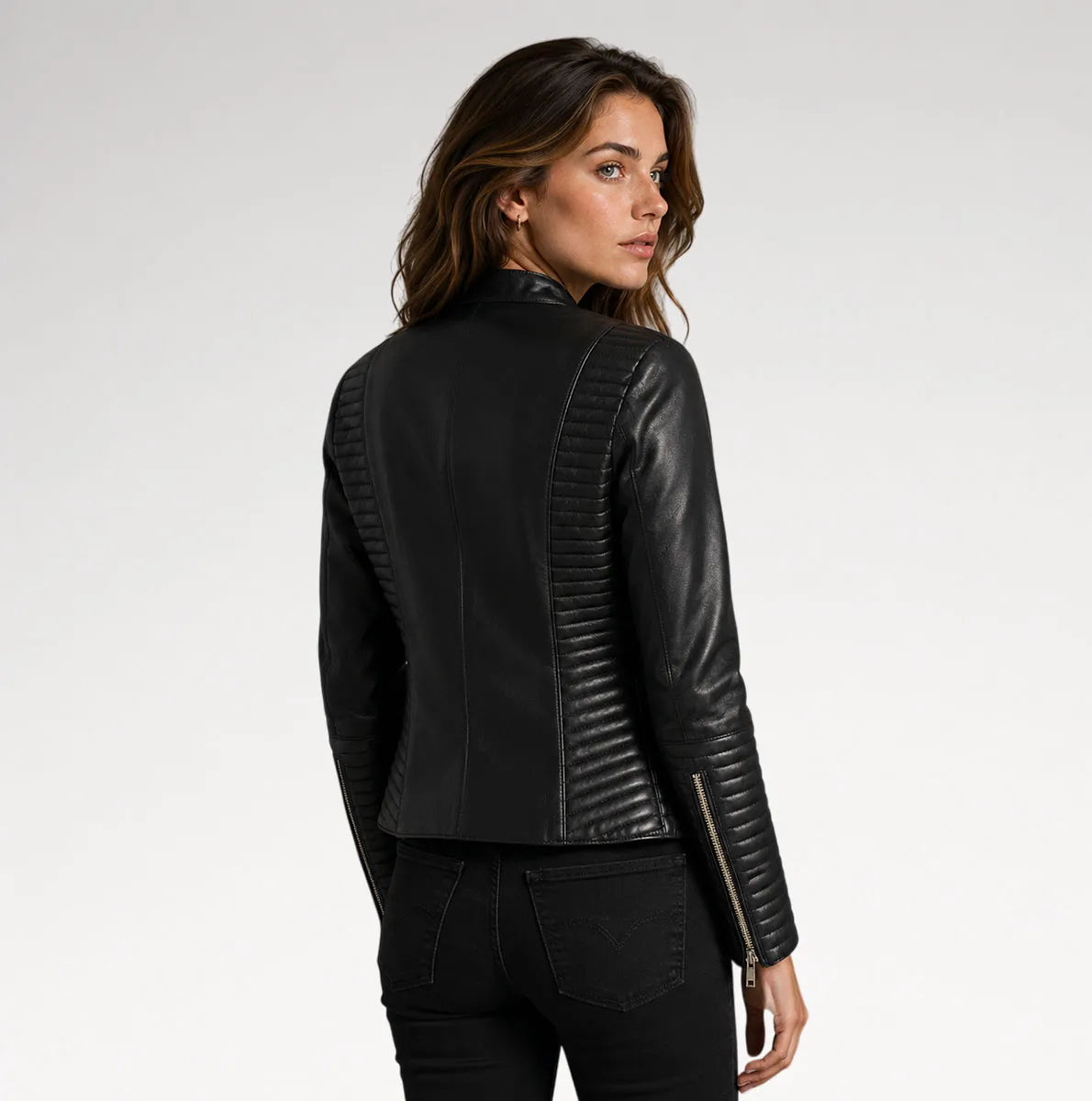 A woman wearing a black leather jacket with quilted back panels and zippered sleeves, shown from a rear three-quarter angle against a light gray studio background.