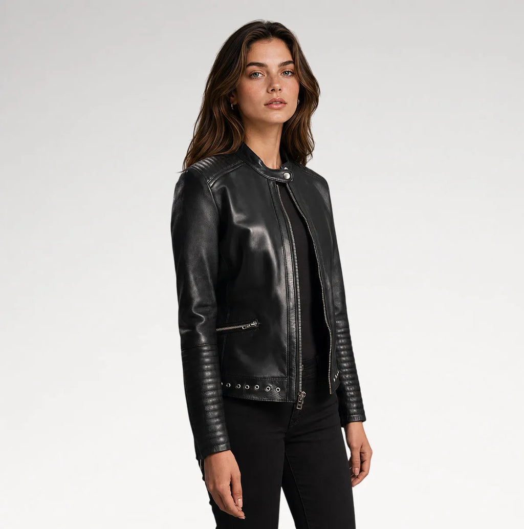 A woman modeling a black leather biker jacket with silver-tone hardware, photographed against a clean light gray studio background.