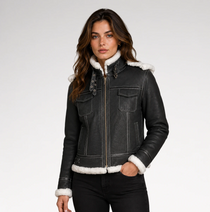 A woman wearing a black leather aviator-style jacket with white shearling lining on the collar, cuffs, and hem, paired with black pants, against a light gray studio background.