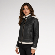 A woman wearing a black leather jacket with white shearling lining on the collar, cuffs, and hem, paired with black pants, photographed against a light gray studio background.
