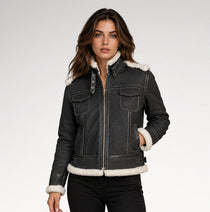 A woman modeling a dark gray denim jacket with a white shearling-style collar, hem, and cuffs, paired with black jeans against a light gray studio background.