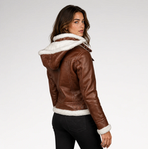 A woman wearing a brown faux-leather hooded jacket with white shearling lining, photographed from the back-three-quarter angle against a light gray studio background.