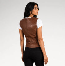A woman shown from the back wearing a brown faux-leather vest over a white short-sleeve t-shirt and black pants, photographed against a light gray studio background.