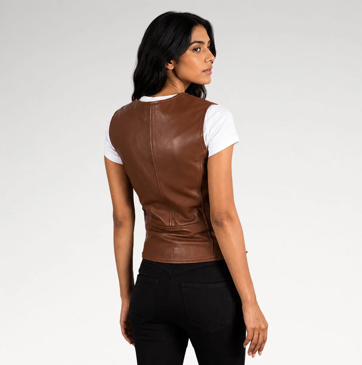A woman shown from the back wearing a brown faux-leather vest over a white short-sleeve t-shirt and black pants, photographed against a light gray studio background.