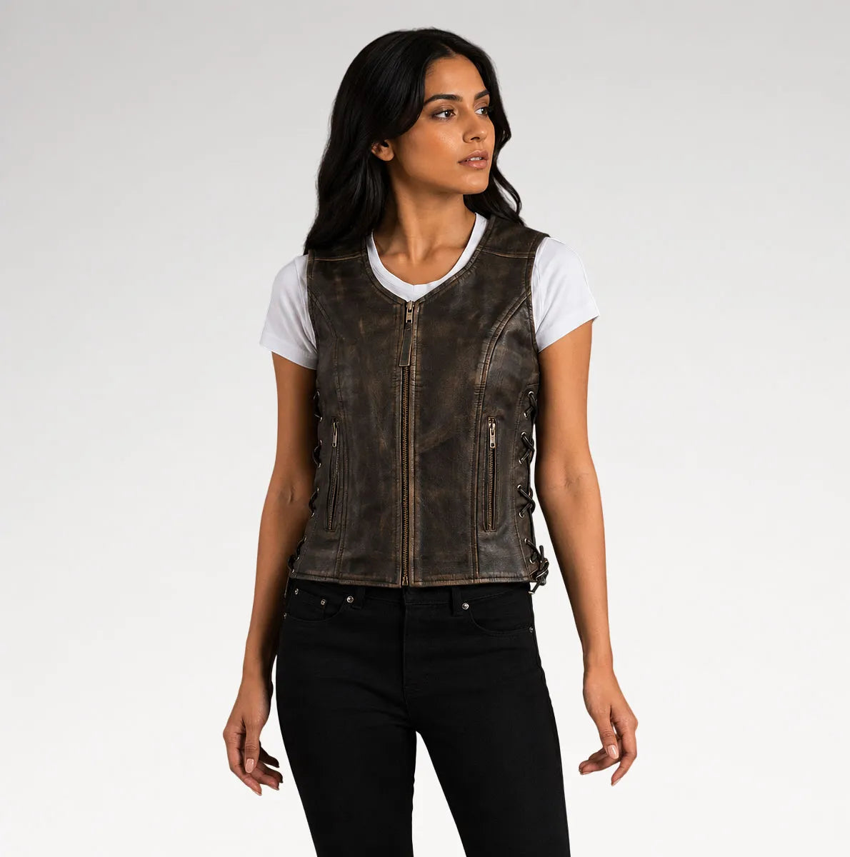 A woman modeling a dark brown distressed leather motorcycle vest over a white t-shirt and black jeans, photographed against a light gray studio background.
