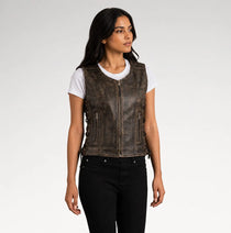 A woman modeling a distressed brown leather motorcycle vest over a white t-shirt and black jeans, photographed against a light gray studio background.