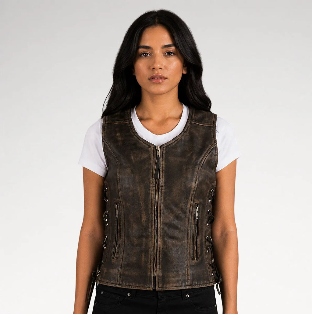 A woman wearing a dark brown distressed leather motorcycle vest over a white t-shirt and black pants, photographed against a light gray studio background.