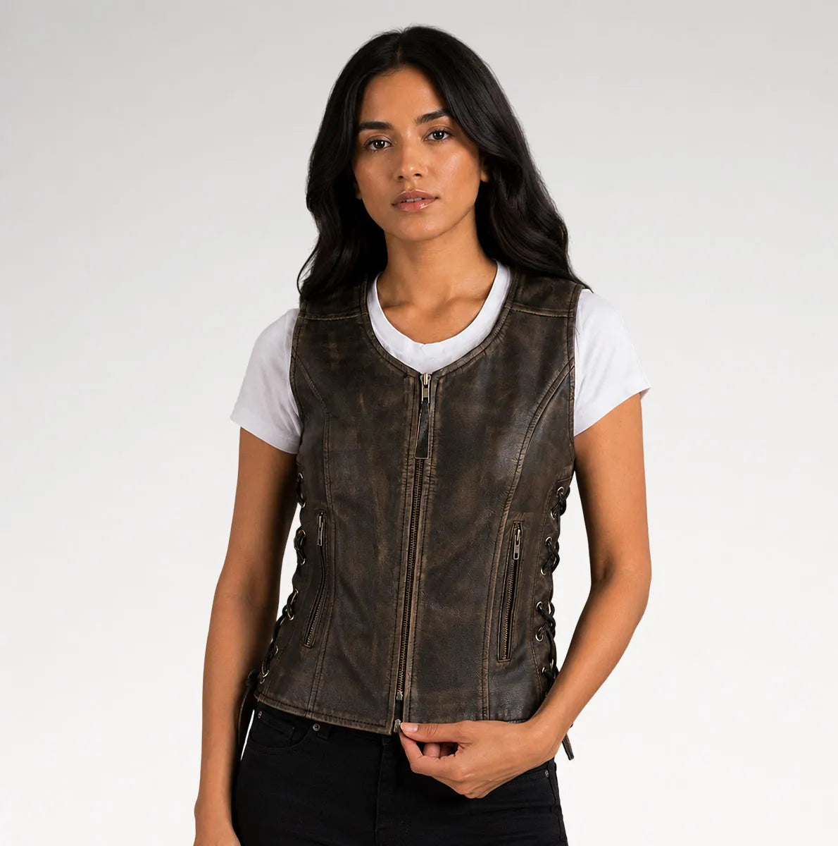 A woman wearing a dark brown distressed leather motorcycle vest over a white t-shirt and black pants, photographed against a light gray studio background.