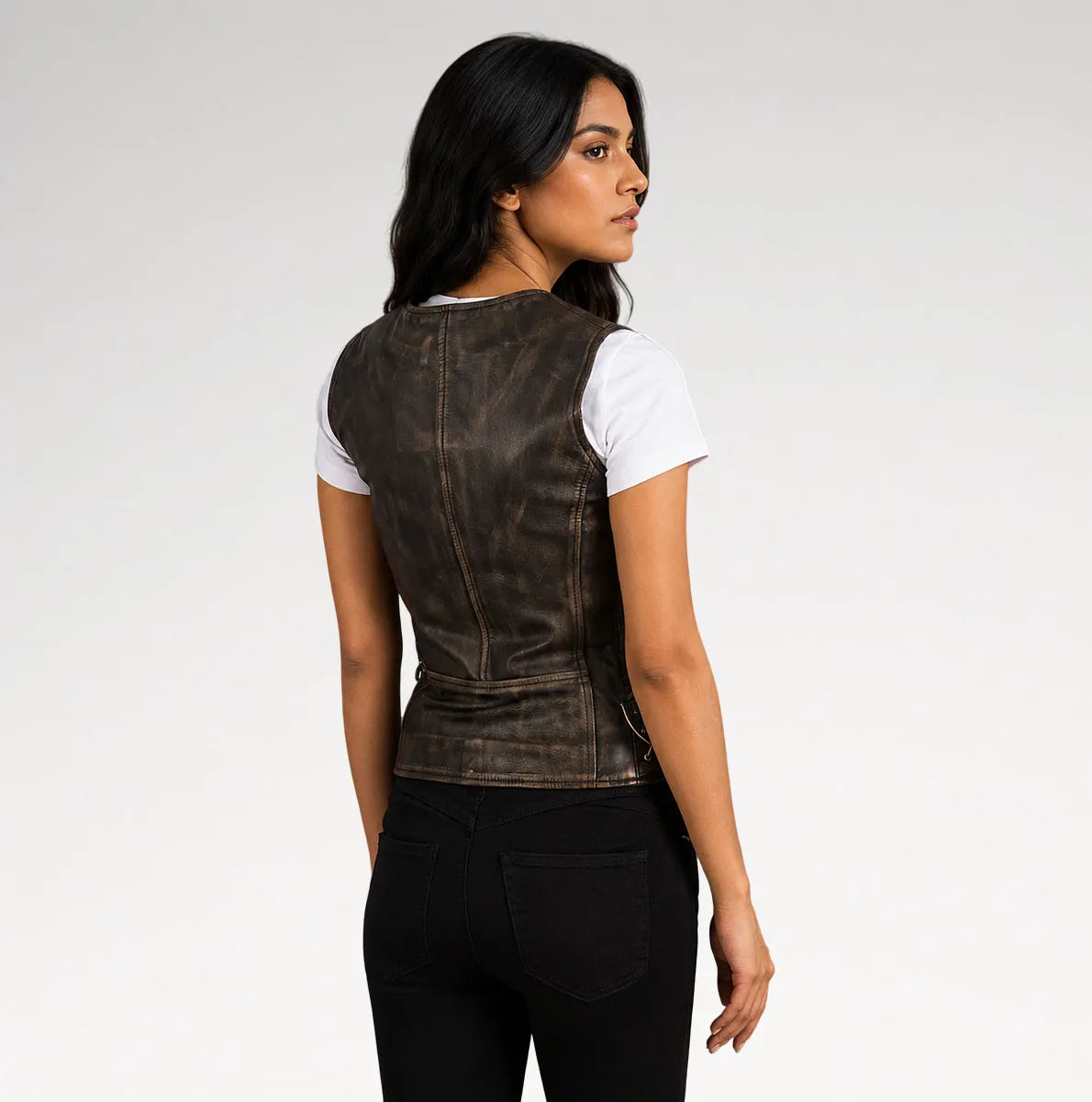 A woman shown from the back wearing a dark brown distressed leather vest over a white t-shirt and black pants, photographed against a light gray studio background.