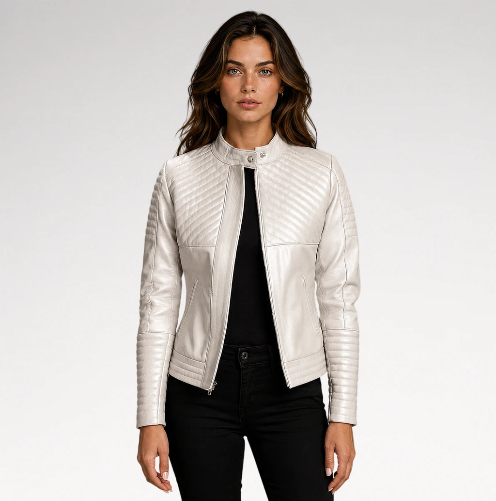 A woman modeling a white faux leather moto jacket with diagonal quilted stitching on the chest and sleeves, paired with a black top and black pants against a light gray studio background.