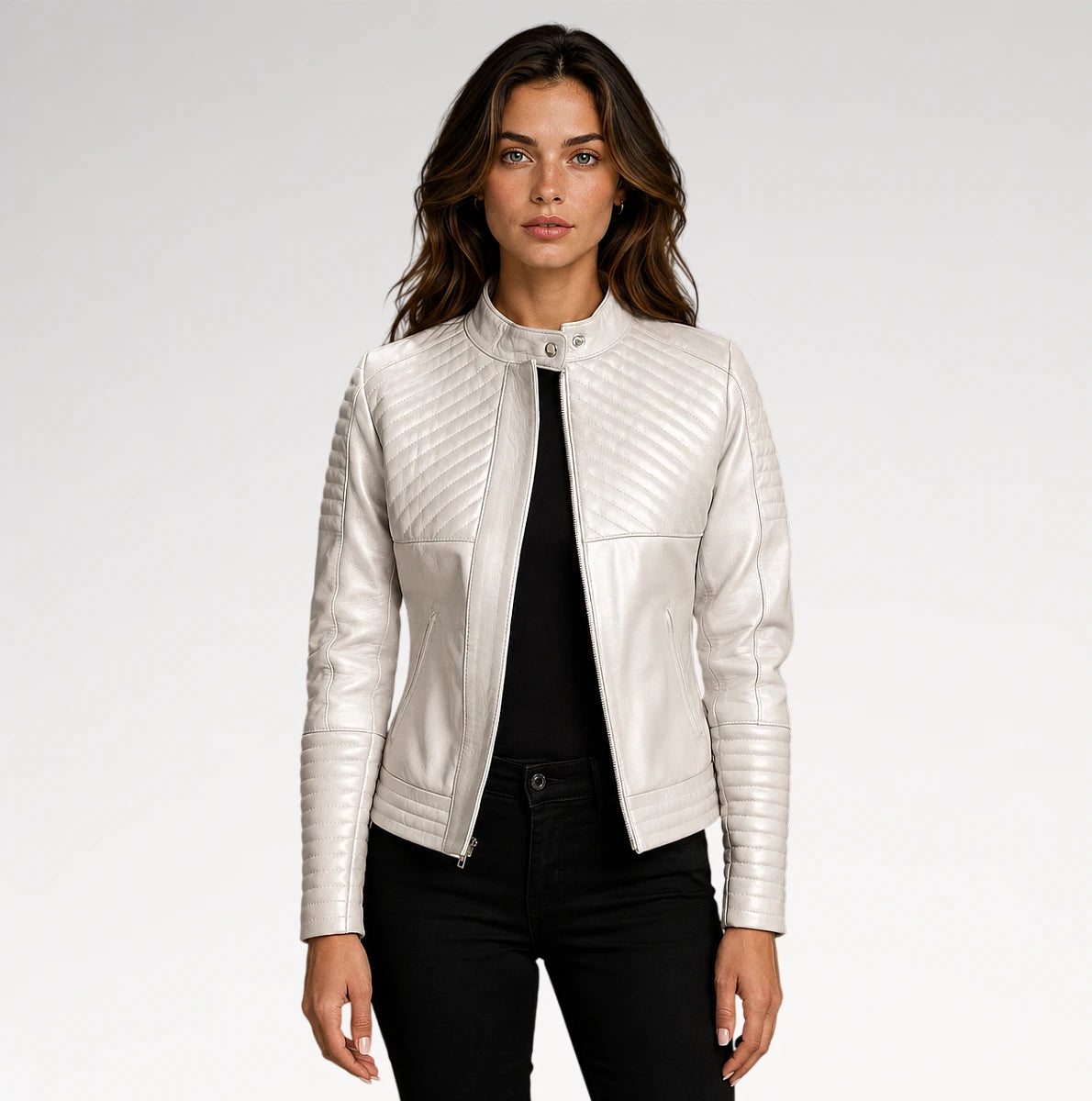 A woman modeling a white faux leather moto jacket with diagonal quilted stitching on the chest and sleeves, paired with a black top and black pants against a light gray studio background.