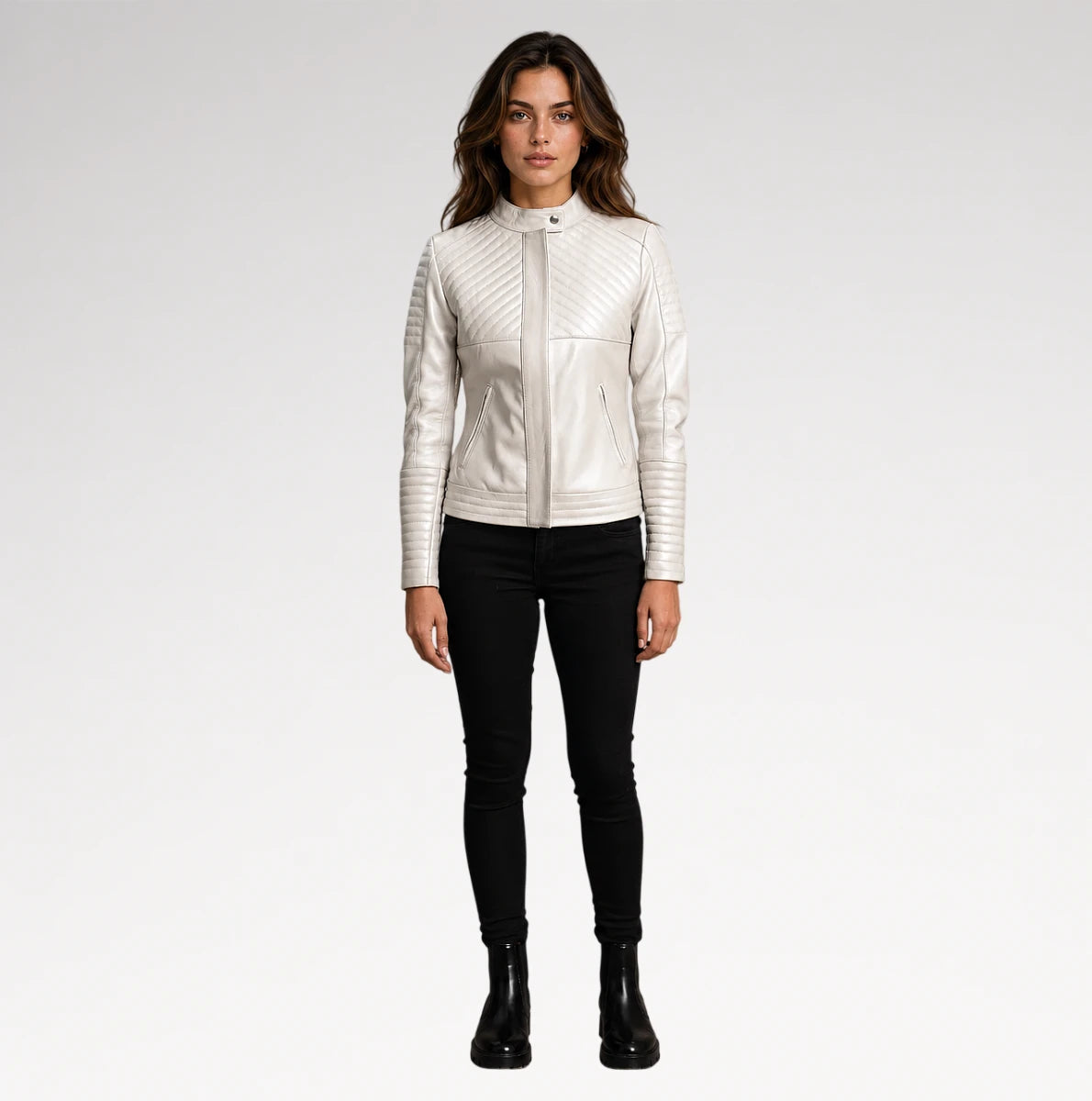 A woman modeling a white faux-leather jacket with diagonal quilted stitching on the chest and sleeves, paired with black skinny pants and black ankle boots, against a light gray studio background.