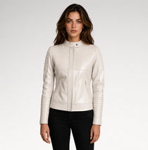 A woman modeling a cream-colored faux leather jacket with quilted diagonal stitching on the chest and sleeves, paired with black pants, against a light gray studio background.