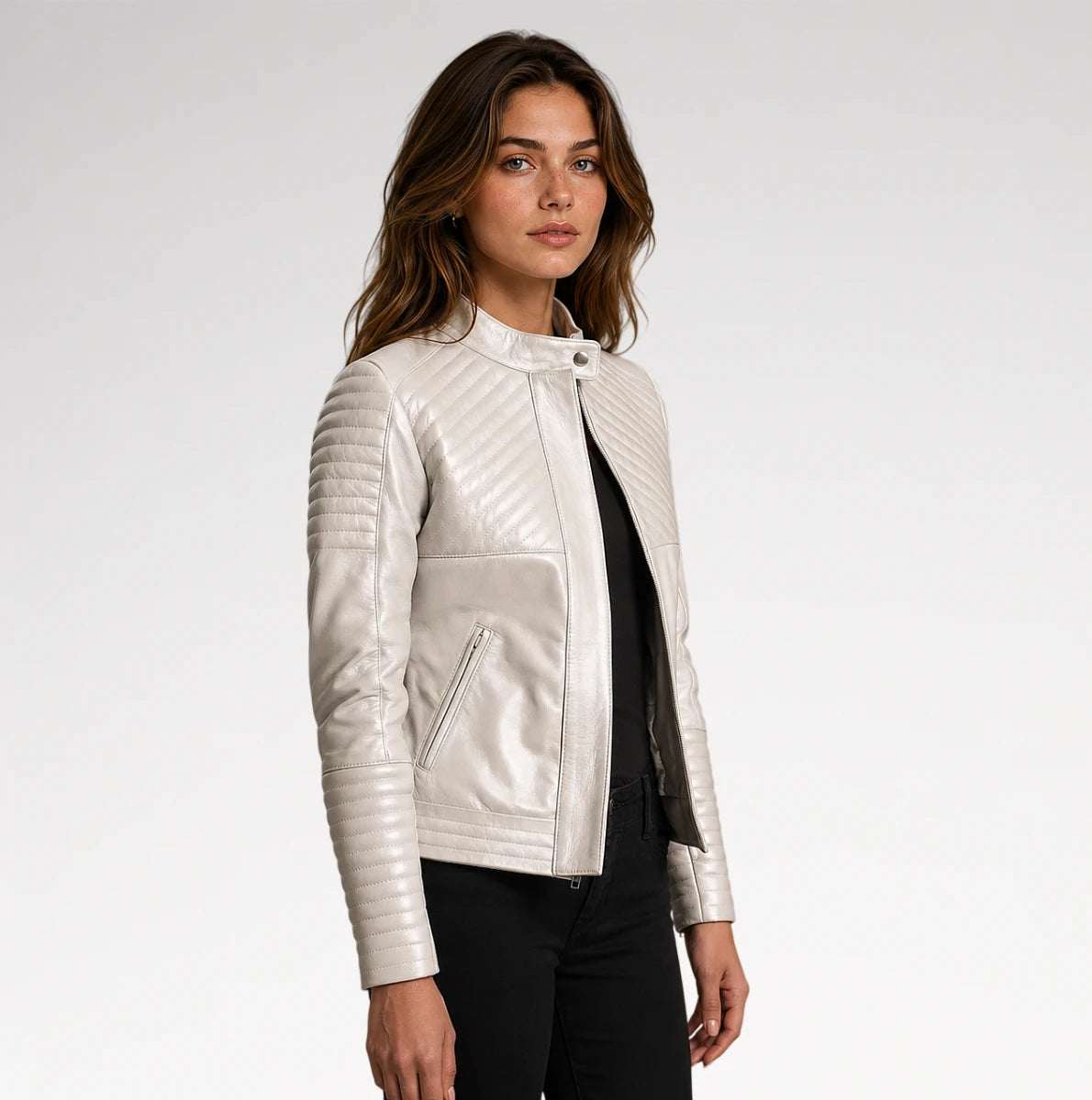 A woman modeling a white quilted faux-leather moto jacket with a stand collar, zippered front, and ribbed sleeves, paired with a black top and black pants against a light gray studio background.